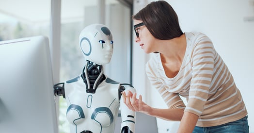 A woman in glasses and a striped shirt interacts with a humanoid robot with digital blue eyes in a modern setting.